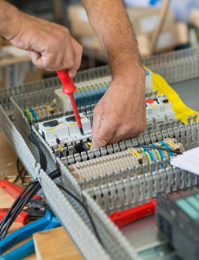 Electrician assembling industrial electric cabinet in workshop.